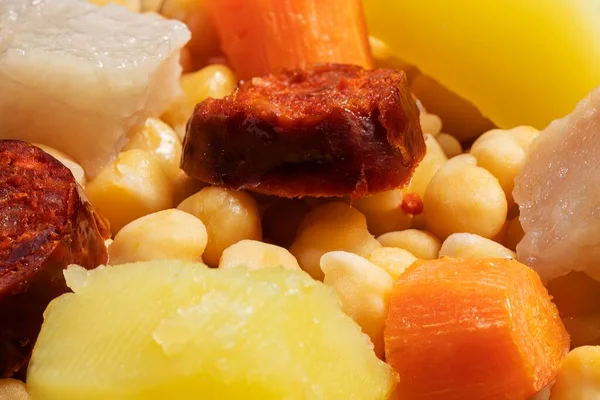 Cooked (Cocido, Guiso) stew, chickpeas with chorizo, bacon, carrot and potato in green saucepan on wooden boards.Concept of traditional Spanish cuisine. Selective focus