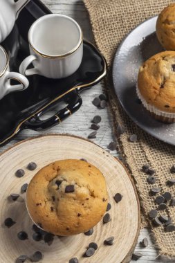 Muffin or cupcake with chocolate chips on wooden table background. Concept of making industrial or homemade pastries. Selective focus.