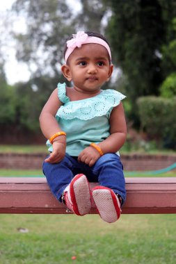 Tahta bir bankta oturan mavi elbiseli bir bebek. Güney Hindistan Bebek Kızı