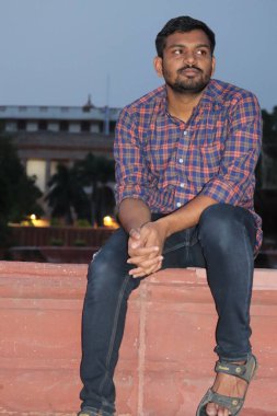 Hindistan, Delhi 'deki Rashtrapati Bhavan binasının önündeki bankta oturan genç Hintli bir adamın portresi.