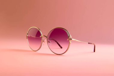 Pembe arka planda altın çerçeveli güneş gözlükleri.