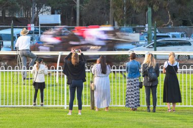 Hipodromda cep telefonlu izleyiciler at yarışını izliyorlar.