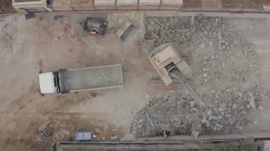 Yıkım alanının hava aracı görüntüsü. Kazıcı kamyona beton ve çelik moloz yüklüyor. Güvenlik donanımlı işçiler.
