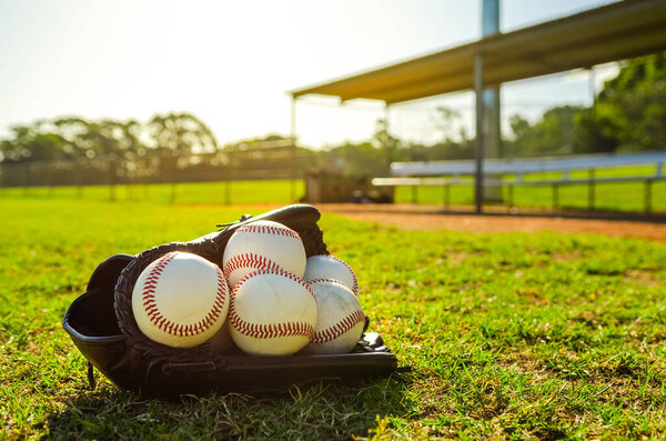 Бейсбольная перчатка, заполненная бейсбольными мячами, сидящими на поле перед пустыми скамейками во время заката