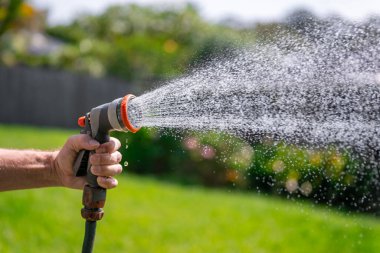 Ayarlanabilir hortumlu bahçe hortumu. Sprey tabanca tutan, çiçekleri sulayan arka bahçedeki çimlere su püskürten bir adam..