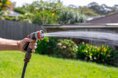 Ayarlanabilir hortumlu bahçe hortumu. Sprey tabanca tutan, çiçekleri sulayan arka bahçedeki çimlere su püskürten bir adam..