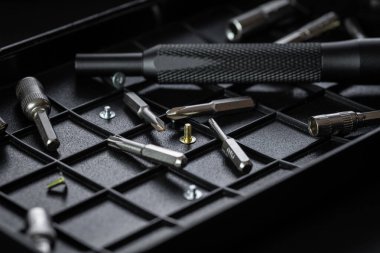 Torx sürücü biti ve alüminyum biti sürücüsü siyah sıralama tepsisinde. Vidalar ve sürücüler etrafa saçılmış. Manyetik prizli tornavida sapı ve kavrulmuş tutuşu.