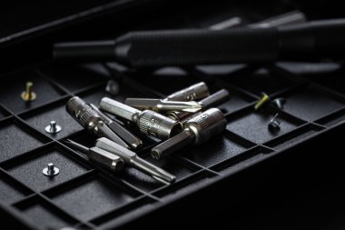 Torx sürücü biti ve alüminyum biti sürücüsü siyah sıralama tepsisinde. Vidalar ve sürücüler etrafa saçılmış. Manyetik prizli tornavida sapı ve kavrulmuş tutuşu.