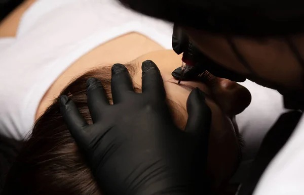 Beauty master in black gloves applying permanent brow tattoo. Closeup shot