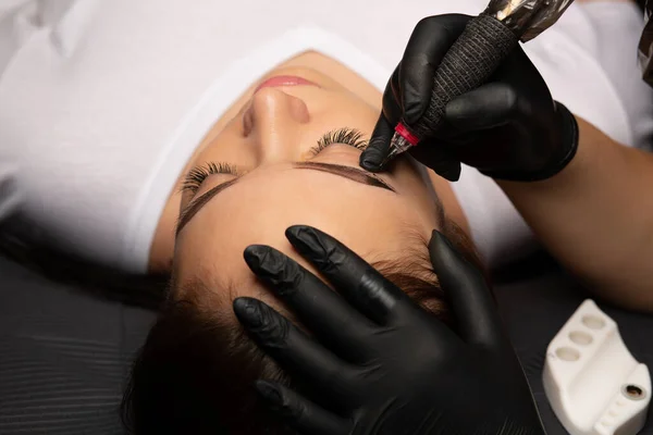 Beauty master\'s hand doing permanent makeup to a pretty woman