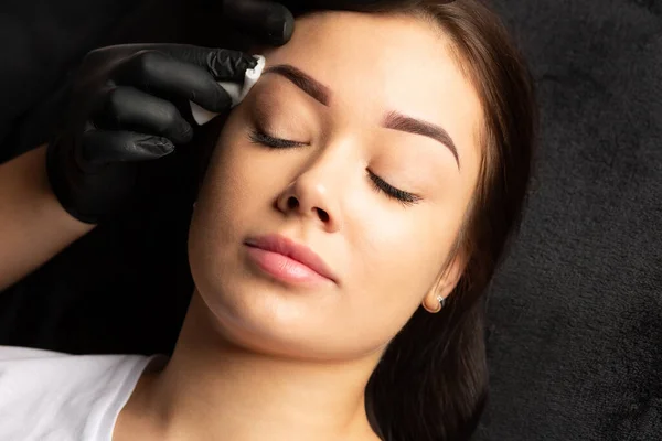 Tattoo master finishing permanent makeup work, cleaning brows with a cotton pad