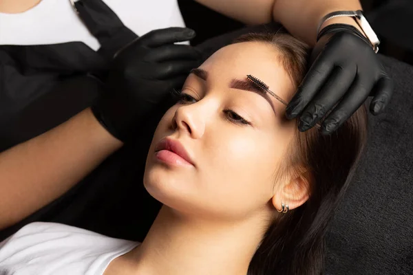 Tattoo master combs eyebrows with a brush after permanent makeup procedure