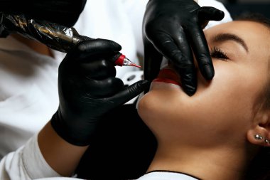 Young woman having lip permanent makeup procedure at beauty salon. Closeup shot
