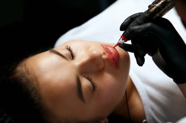 Young woman having lip permanent makeup procedure at beauty salon. Closeup shot