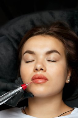 Young woman having lip permanent makeup procedure at beauty salon. Closeup shot
