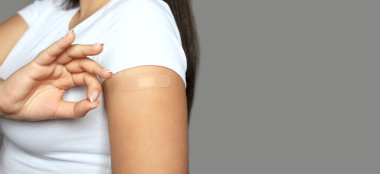 Young woman with a medical plaster on her arm after vaccination. Closeup shot