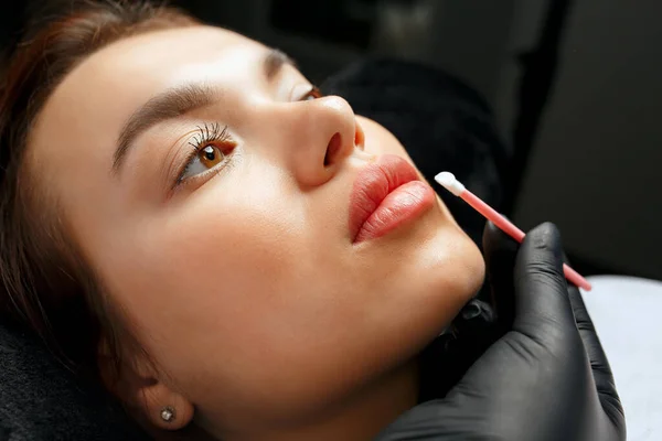 Lip care after the permanent make-up procedure: beauty master applying gel to a woman\'s lips