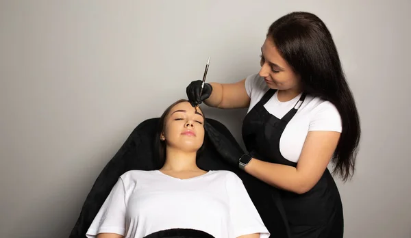 Beauty master correcting eyebrow shape with a pencil before permanent makeup