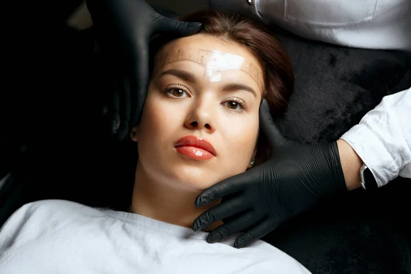 Cosmetician measuring the angle and forming the shape of the eyebrows during the permanent tattoo procedure