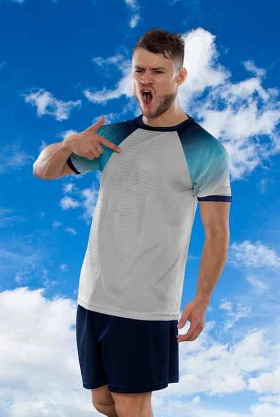 イングランド代表チームの白いTシャツを着たプロのサッカー選手は 雲の中で空を背景に反抗と幸福の表現でゴールを決めたことに興奮して叫んでいます — ストック写真