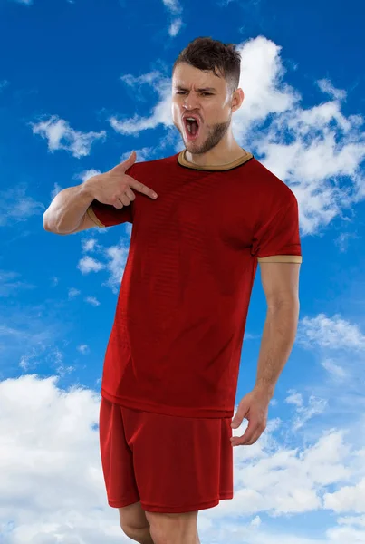 セルビア代表チームの赤いTシャツを着たプロのサッカー選手は 雲の中で空を背景に反抗と幸福の表現でゴールを決めたことに興奮して叫んでいます — ストック写真