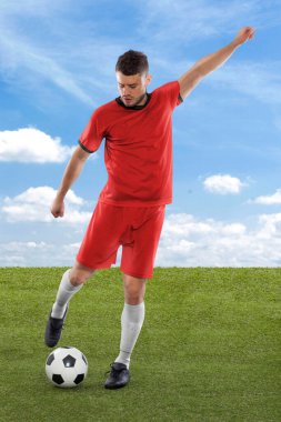 Kırmızı Kore Cumhuriyeti milli takımının formasına sahip profesyonel futbolcu sahadaki çimenler ve bulut arka planı üzerinde meydan okuma ve karar ifadesiyle gol atmak üzere.