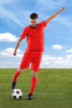 Kırmızı Danimarka milli takımının formasına sahip profesyonel futbolcu sahadaki çimenler ve bulut arka planında yüzüne meydan okuma ve karar ifadesi ile gol atmak üzere.