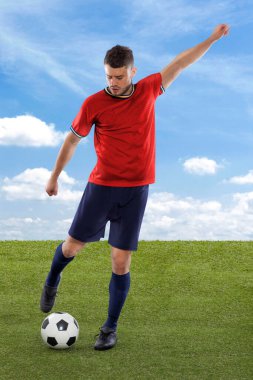Kırmızı İspanya milli takımının formasına sahip profesyonel futbolcu sahadaki çimenler ve bulut arka planında yüzüne bir meydan okuma ve karar ifadesi ile gol atmak üzere.