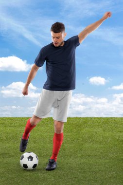 Mavi Fransa milli takımının formasına sahip profesyonel futbolcu sahadaki çimenler ve bulut arka planında yüzüne bir meydan okuma ve karar ifadesi ile gol atmak üzere.