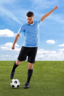 Uruguay Millî Futbol Takımı forması ile profesyonel futbolcu sahadaki çimenler ve bulut arka planında meydan okuma ve karar ifadesiyle gol atmak üzere.