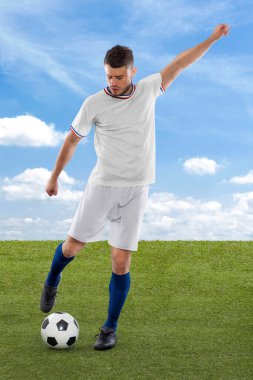 Amerikan milli takımı forması olan profesyonel futbolcu sahadaki çimenler ve bulut arka planı üzerinde meydan okuma ve karar ifadesiyle gol atmak üzere.