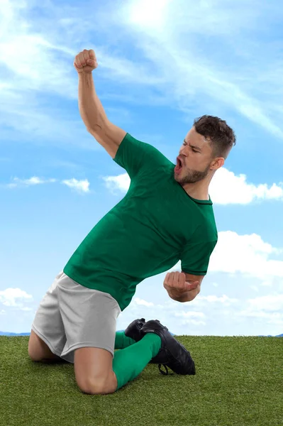 拥有绿色的沙特阿拉伯国家队球衣的职业足球运动员兴奋地大喊 因为他们在场上的草地和云彩背景下 用一种挑战和快乐的表情射门 — 图库照片