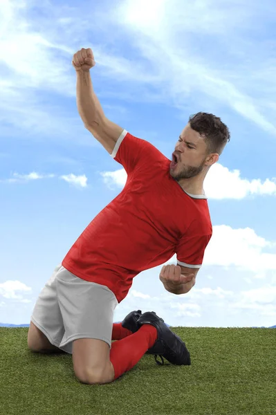 一名职业足球运动员 身穿红色的突尼斯国家队球衣 兴奋地大喊着 因为他在场上的草地和云彩背景下 用一种挑战和快乐的表情射门 — 图库照片