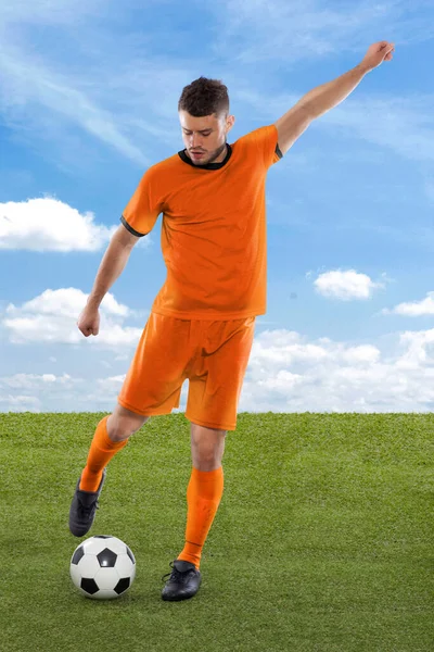 Professional soccer player with orange Netherlands national team jersey about to score a goal with an expression of challenge and decision on his face on field grass and cloud background