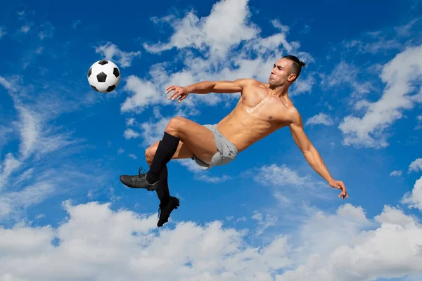 Athletic man without jersey soccer player jumping about to kick the ball on sky and clouds background.
