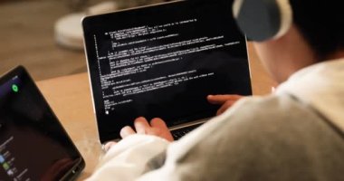 Young man with headphones sitting on the floor of his house studying and working at home with a computer, tablet, book, cell phone and glass of water.