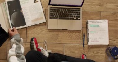 Young man with headphones sitting on the floor of his house studying and working at home with a computer, tablet, book, cell phone and glass of water.