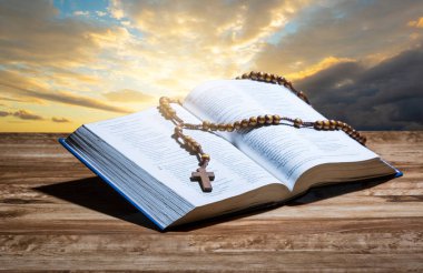 Hopen holy bible and rosary on wooden table and sunset background.