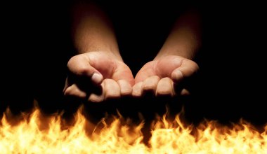 Closed man hands over hell flames on black background.