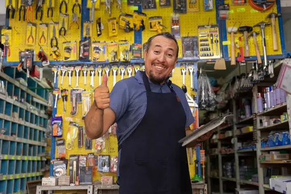 Handsome adult entrepreneur man in apron, with an expression of pride and happiness in her business full of hardware products.