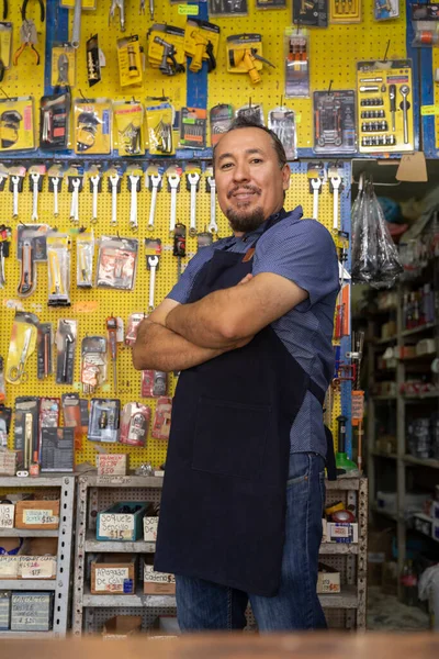 Handsome adult entrepreneur man in apron, with an expression of joy and happiness in her business full of hardware products.
