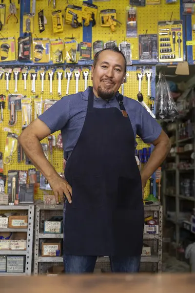 Handsome adult entrepreneur man in apron, with an expression of joy and happiness in her business full of hardware products.