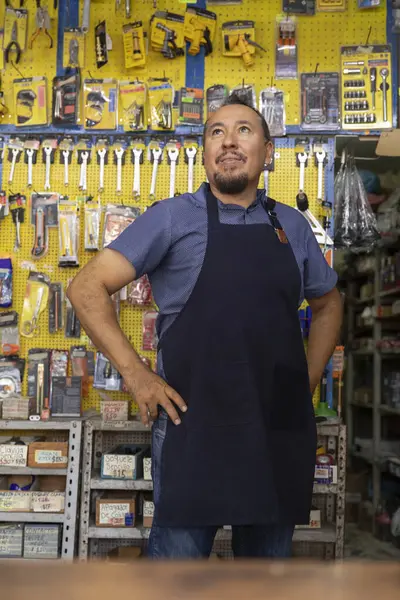 Handsome adult entrepreneur man in apron, with an expression of joy, happiness and proud in her business full of hardware products.