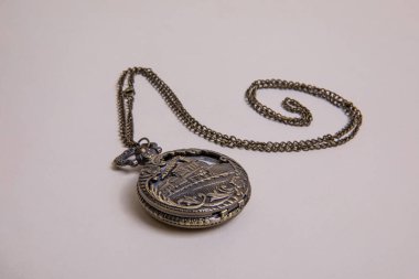 Kapağında tren gravürü olan eski bir cep saati, patentli broşür rengi, bej arka plan görünümünde bir spiral şeklinde dizilmiş zincir ile kapalı.