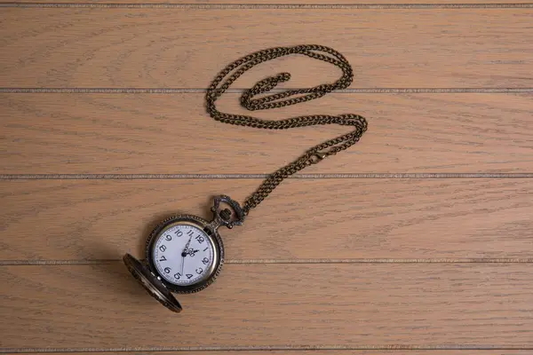 stock image antique pocket watch with train engraving on the front cover, patinated brobce color, chain arranged in a spiral on a wooden background