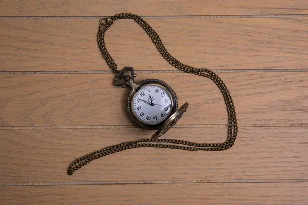 stock image antique pocket watch with train engraving on the front cover, patinated brobce color, chain arranged in a spiral on a wooden background