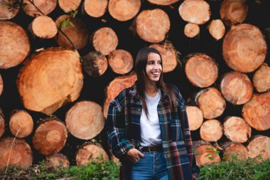 Yığılmış ağaç gövdelerinin yanında gülümseyen genç bir kız. Kavram çevresi, sürdürülebilirlik, doğa, ormansızlaşma.