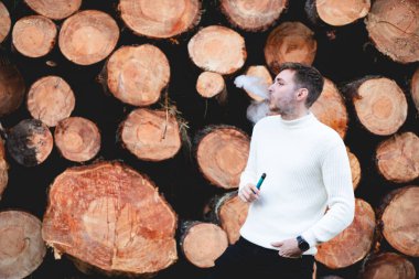 Vaper içen, tahta kütüklerin yanında buharlaşan genç bir çocuk. Sağlık konsepti, buhar..