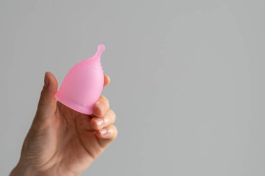 Kadının elinde tekrar kullanılabilen pembe bir adet kupası. Kadın sağlığı konsepti, sıfır tüketim, ped ve tampona alternatif. Metin için yer