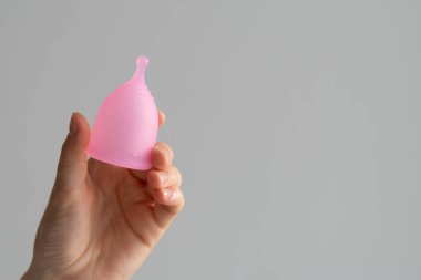Tecrit edilmiş bir zemindeki kadının ellerinde pembe regl kupası. Adet ve kritik günlerin teması.